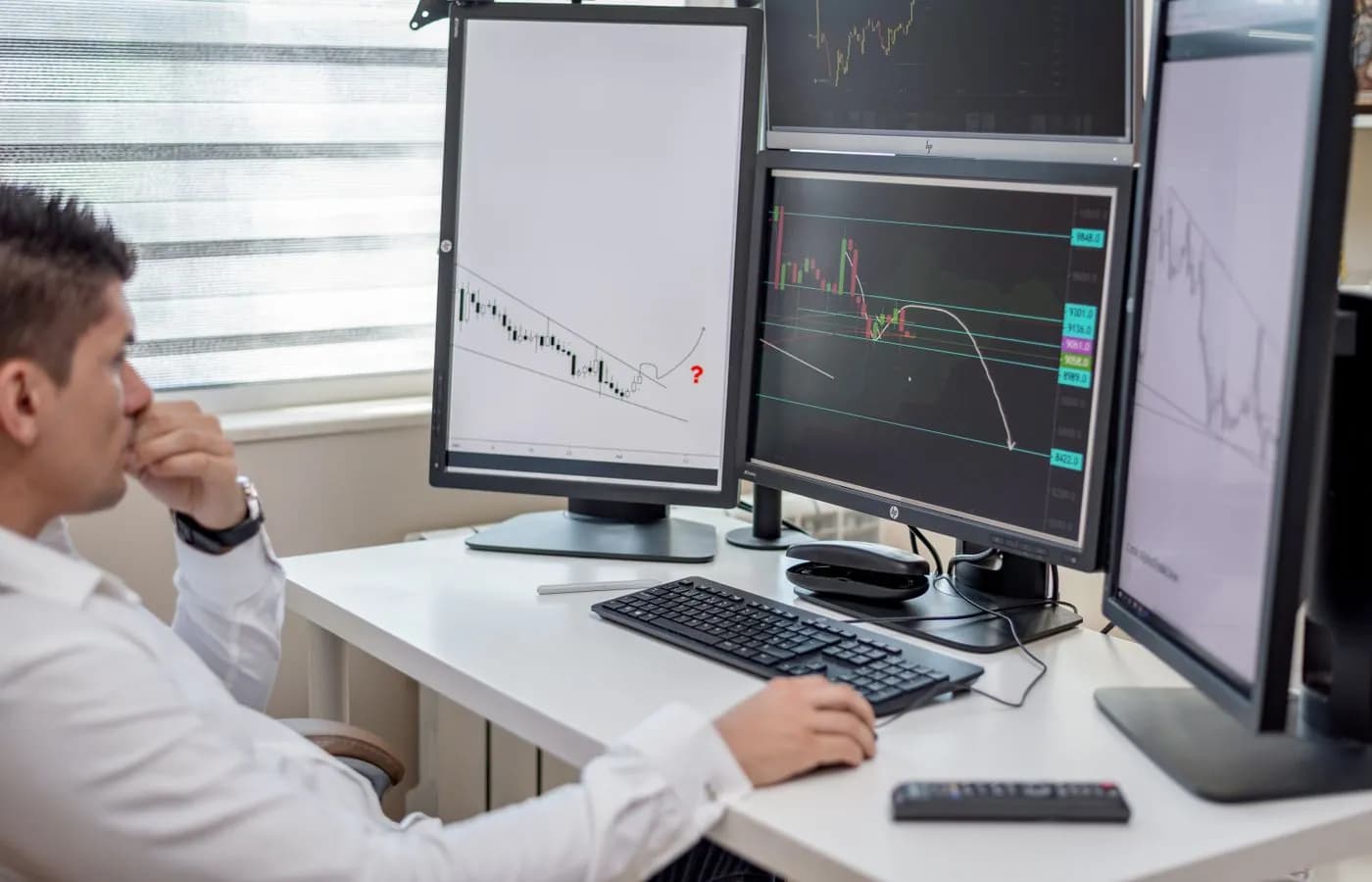 Analista financeiro a estudar gráficos em vários monitores, num escritório escuro